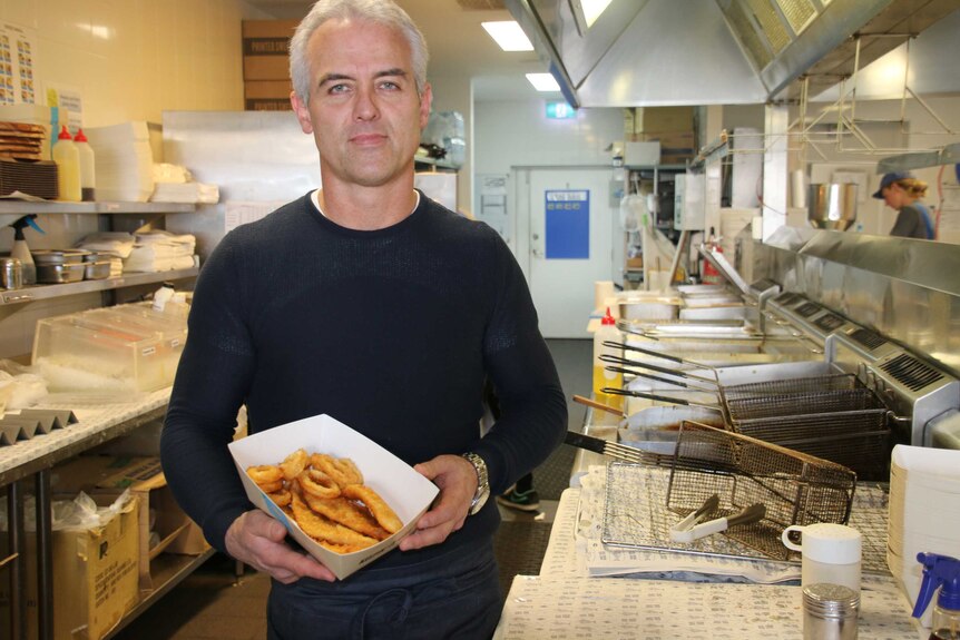 A mid shot of Michael Waldock standing in the kitchen of a fish and chip restaurant holding a seafood basket.