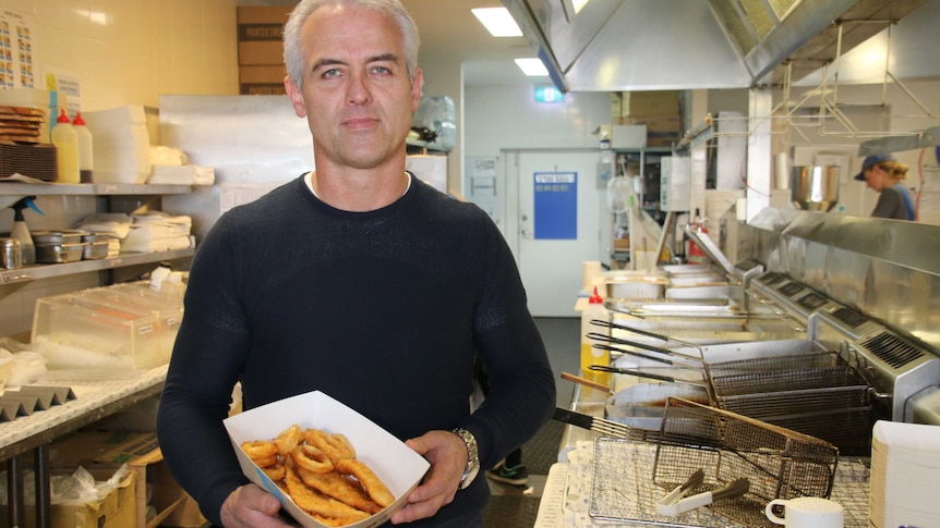 A mid shot of Michael Waldock standing in the kitchen of a fish and chip restaurant holding a seafood basket.