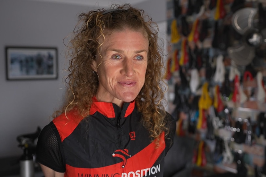 A woman with curly hair in cycling gear smiles.