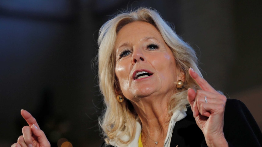 A blonde women points her two index fingers up while making a point in a speech