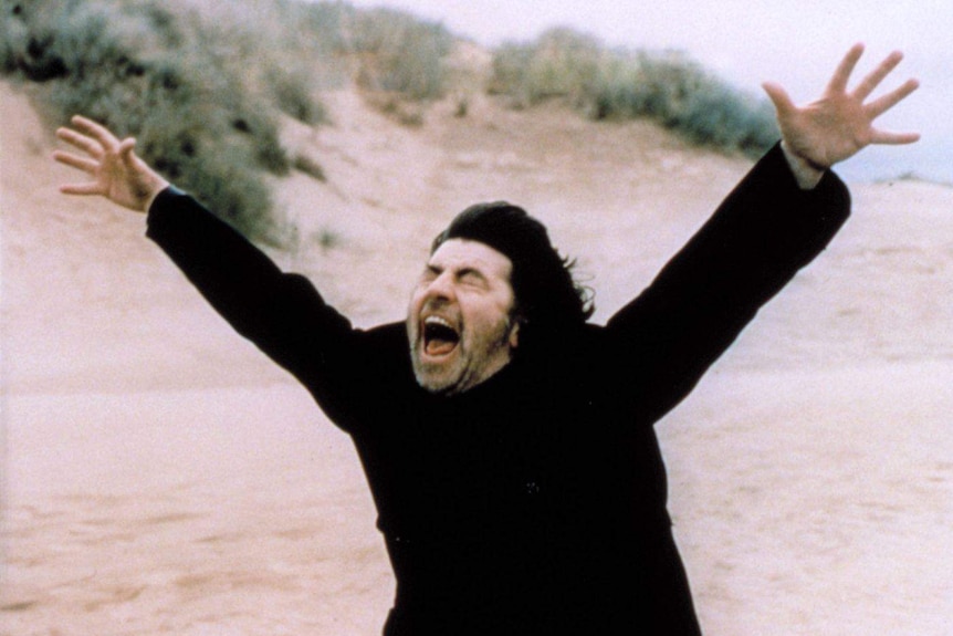 A man in black arms outstretched shouting in the film The Shout