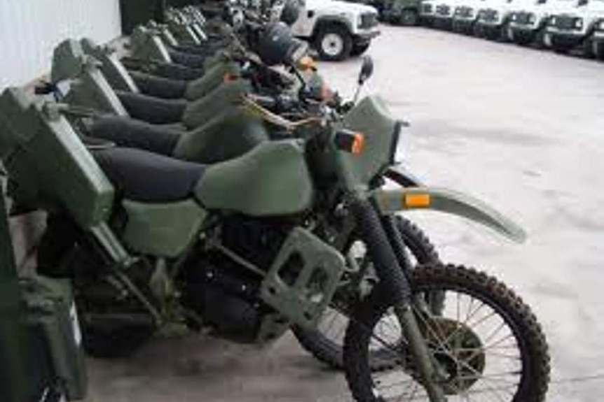 A dozen green military trial bikes and white Jeeps parked at an army base