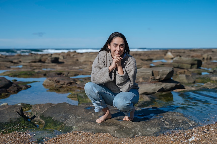 A young woman crouching on the rocks at the beach