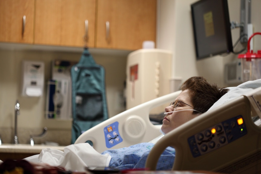 A woman lays in a hospital bed with oxygen tubes. 