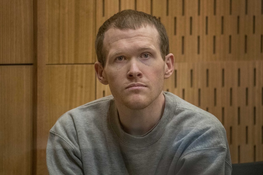 Brenton Tarrant in a grey sweatshirt sitting in a court room