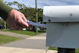 A hand putting a piece of paper into a residential letterbox.