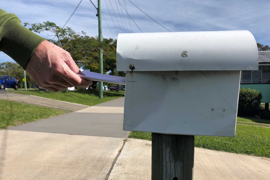 A hand putting a piece of paper into a residential letterbox.