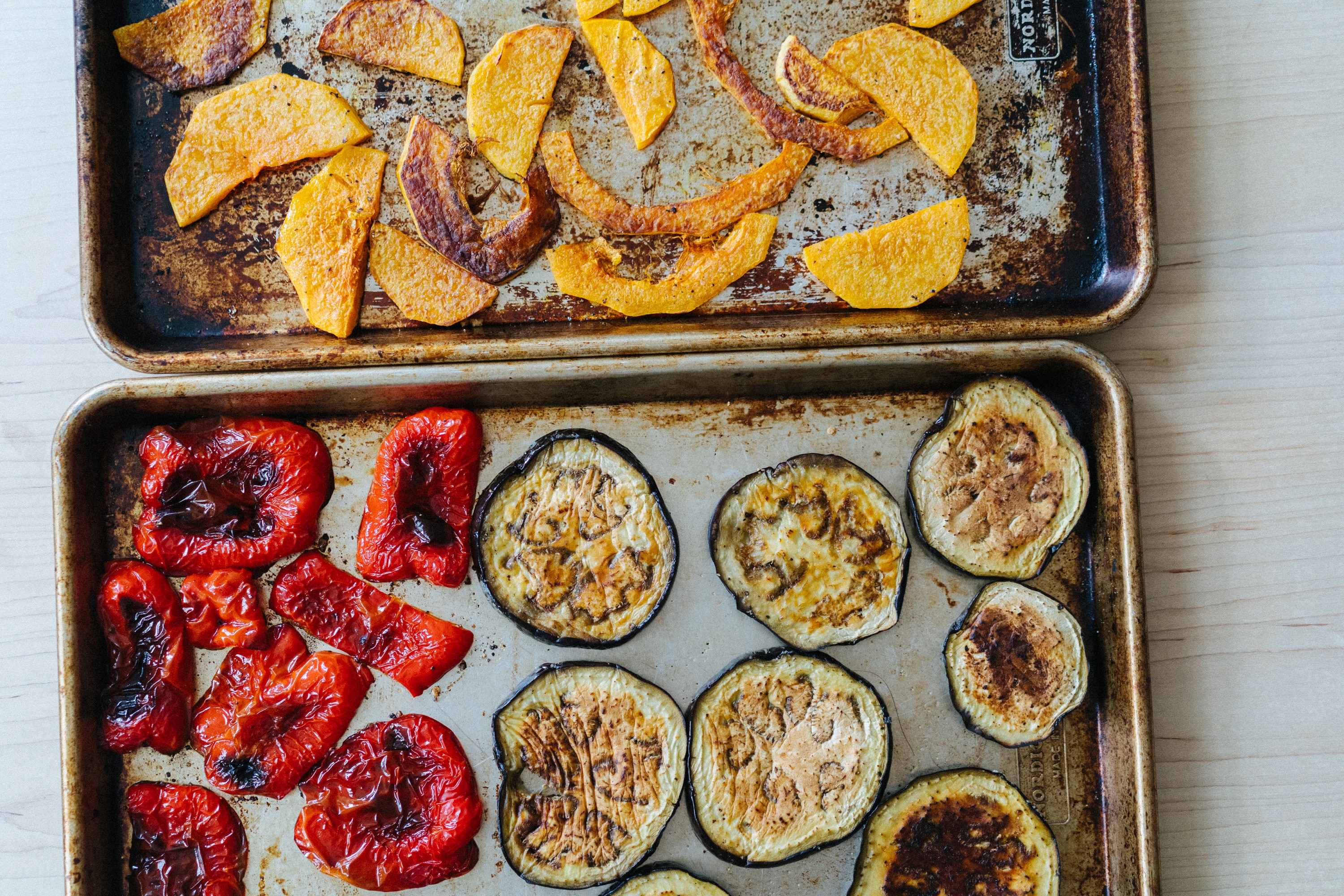 Roasted pumpkin, red capsicum and eggplant on two baking trays lined with paper.