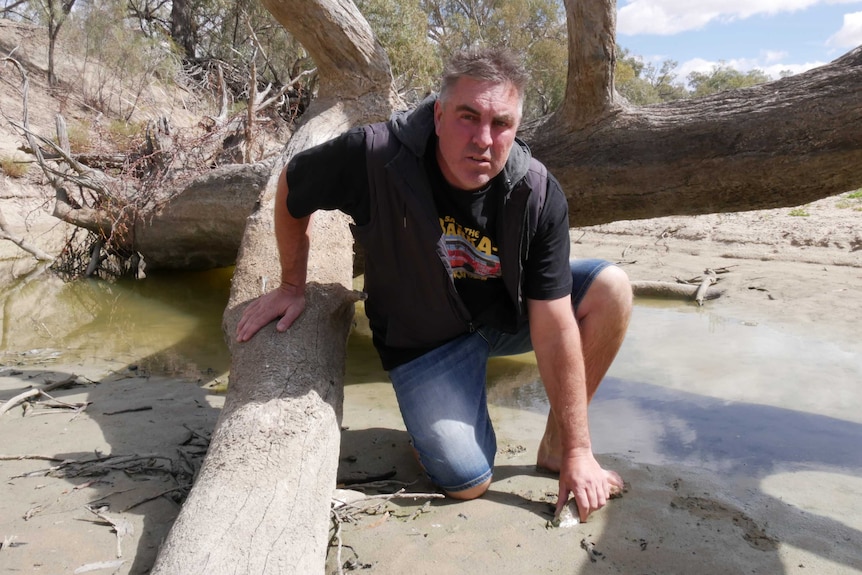 A man kneels next to a shallow pool of water on the Darling River.