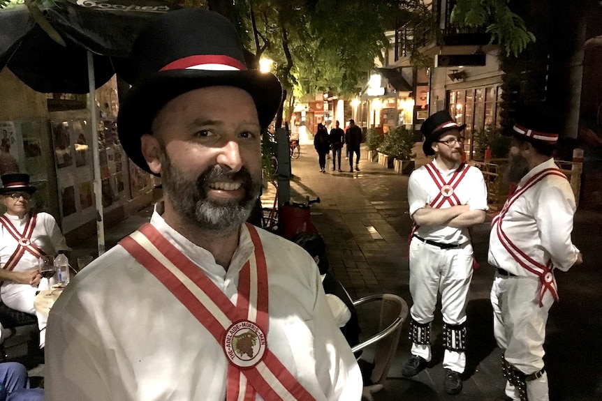 A man wearing a top hat outside a pub smiles at the camera