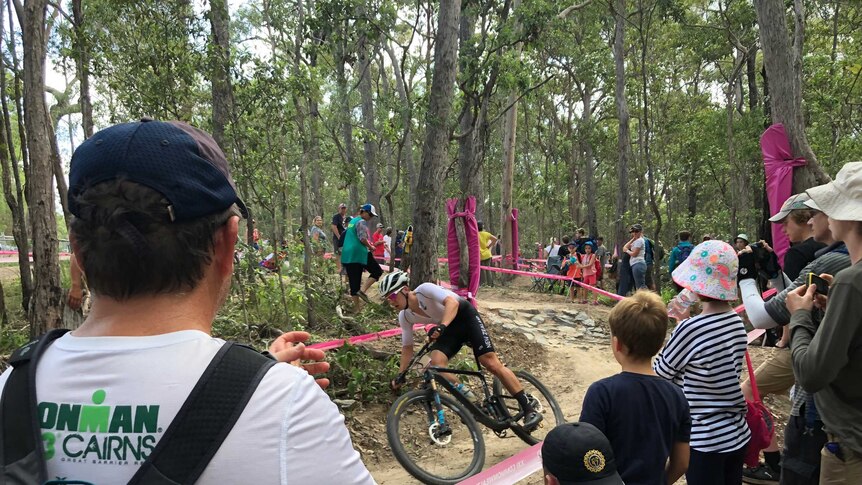 A man looks towards to mountain bike trail and claps as a rider from New Zealand whips by.