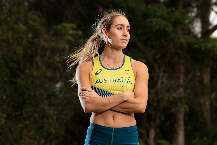 Sarah Carli stands with her arms folded while wearing a gold Australia running top and green shorts.