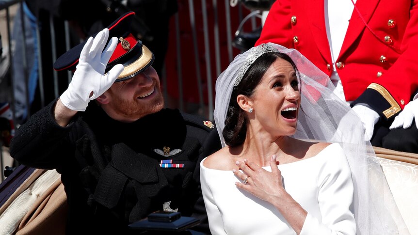 Britain's Prince Harry and his wife Meghan ride a horse-drawn carriage.