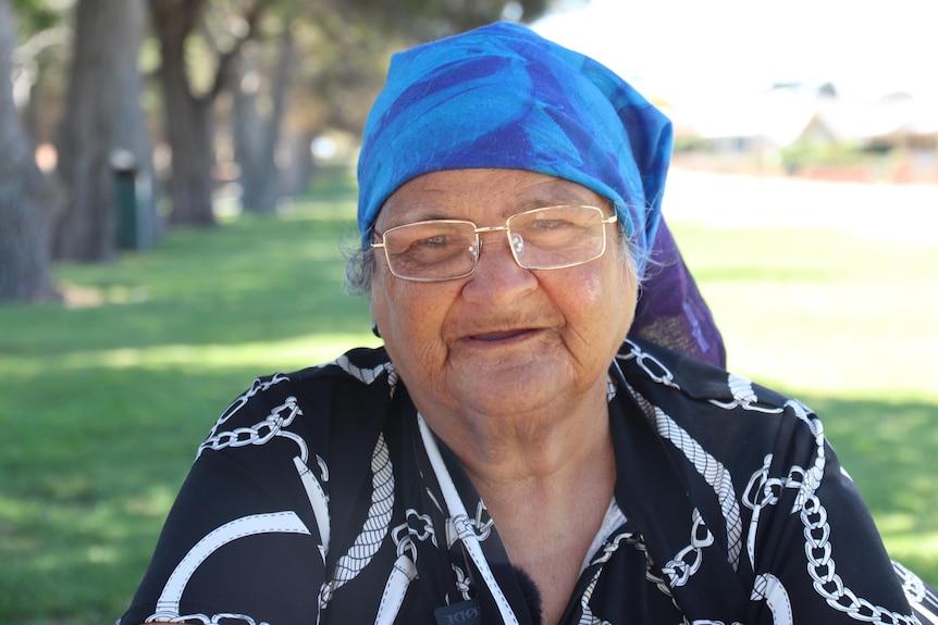 Elderly indigenous lady in blue headscarf with lawn and trees blurred in the background