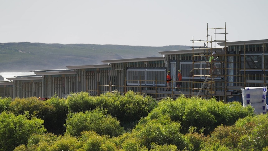 Three people wearing high vis on a building site with ocean and hills in the background