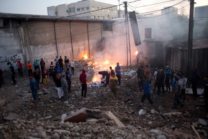Palestinians stand among rubble and small fires to check the damage from Israeli airstrikes in Gaza city.