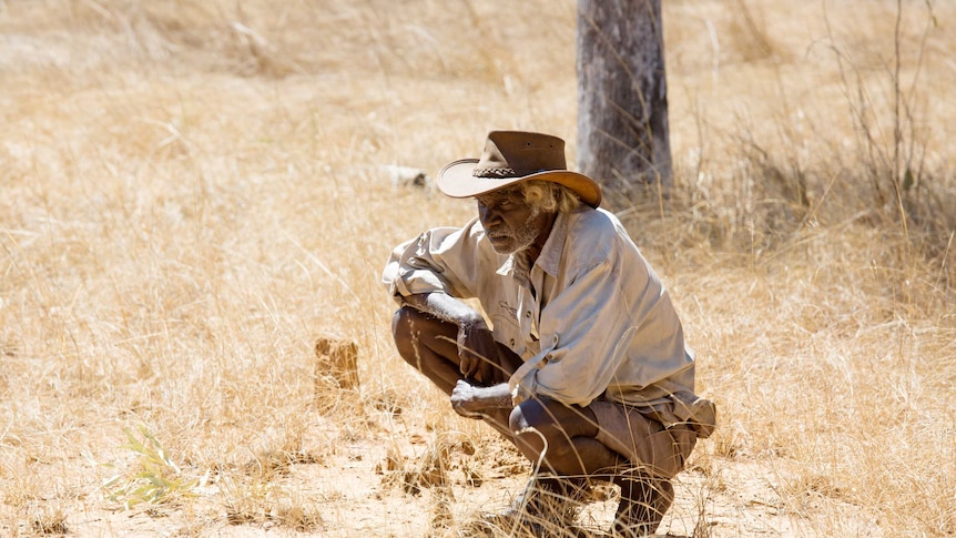 Central Arnhem Land traditional owner Robert Redford is kneeling amongst dried grass in central Arnhem Land.