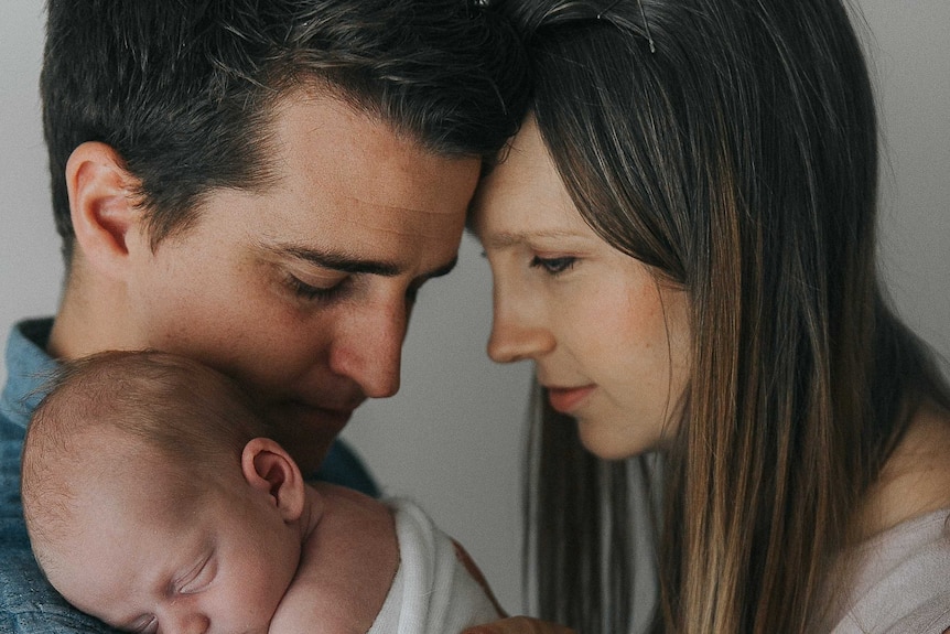 Man and woman, heads touching, holding a tiny baby