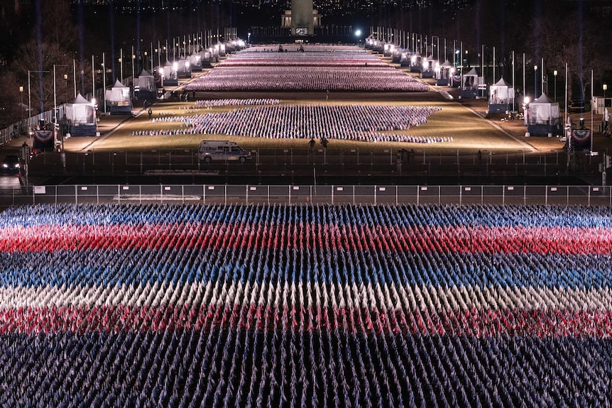 thousands of flags stand along a road with tents on either side.