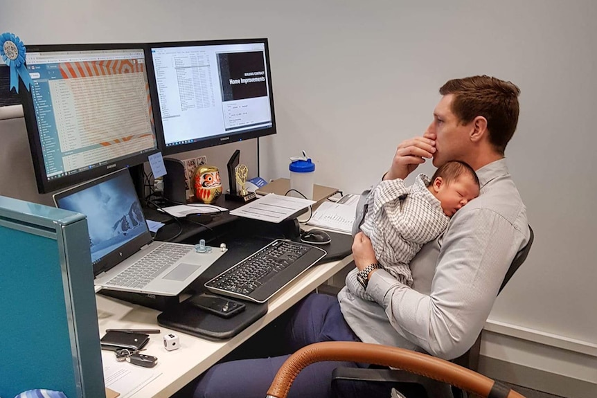 Father sitting at his desk working while holding his baby son.