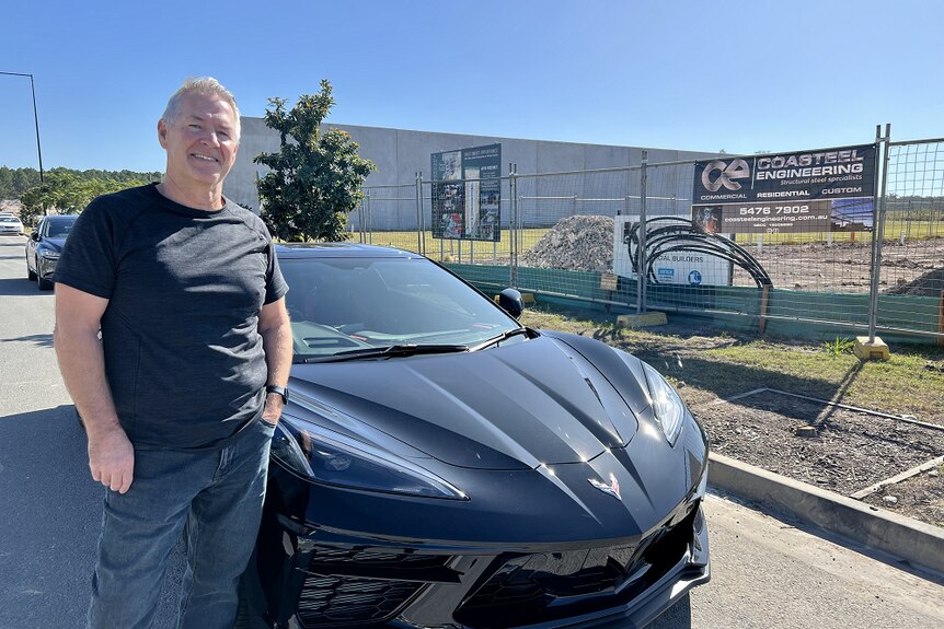 Man in a black shirt and jeans, standing beside a black corvette