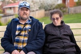 A woman and her father sit on a bench waiting for a bus.