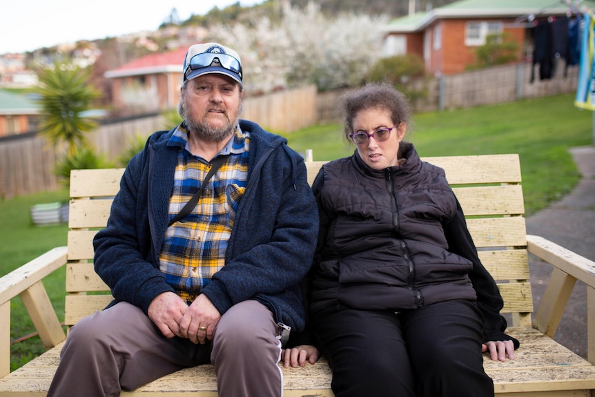 A woman and her father sit on a bench waiting for a bus.