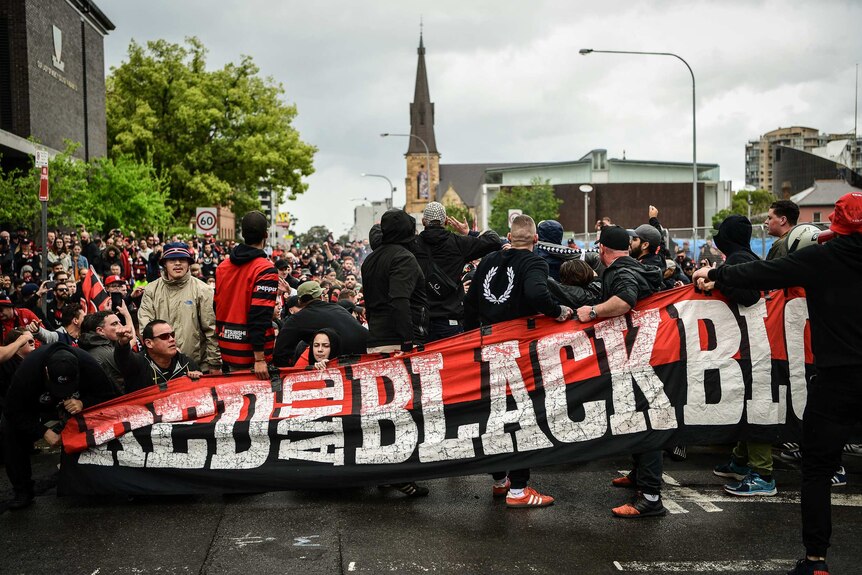 A banner with the words "Red and Black Bloc" is held across the front of a parade of people.