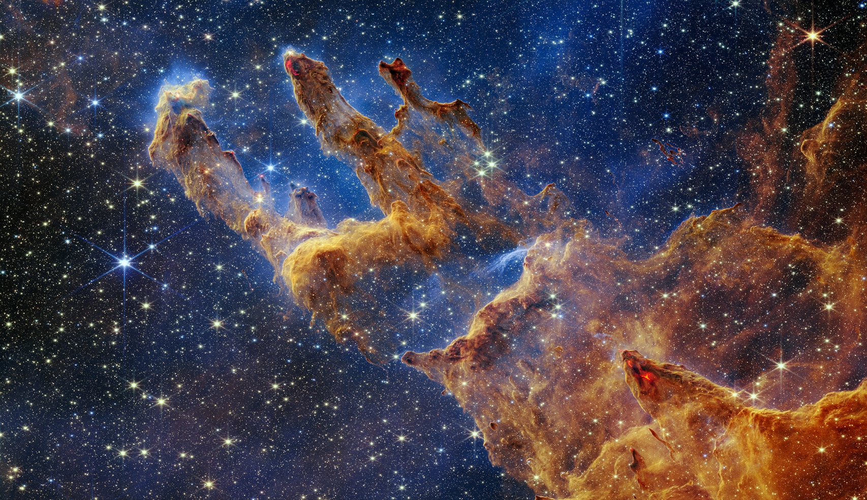 A sea of yellow and white stars against a dark blue background and three rock-light formations made of dust, orange in colour. 
