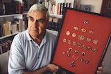 Graham 'Polly' Farmer holds up a frame with his best and fairest medals along with his MBE.