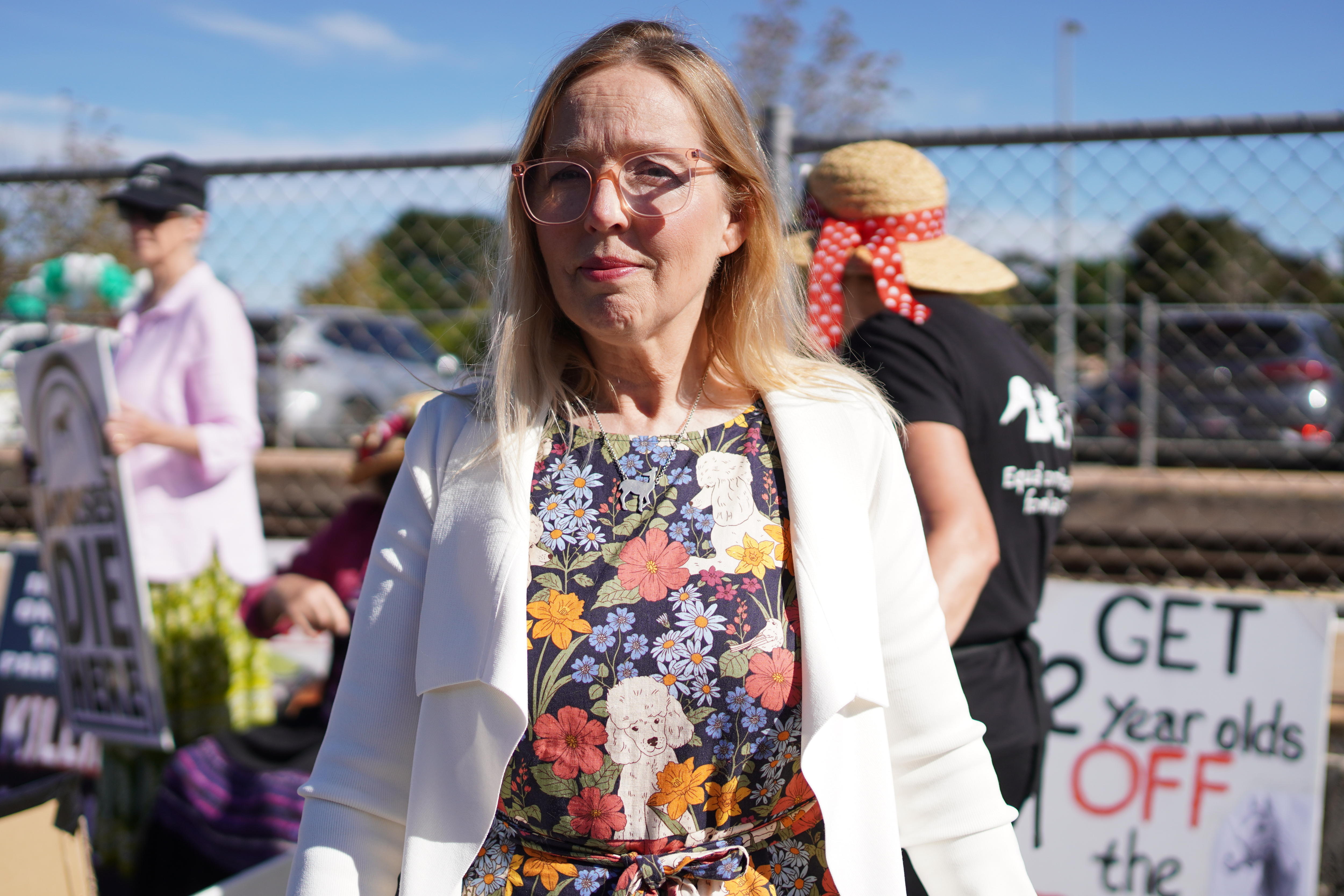 A woman stands in front of placards at a protest against horse racing
