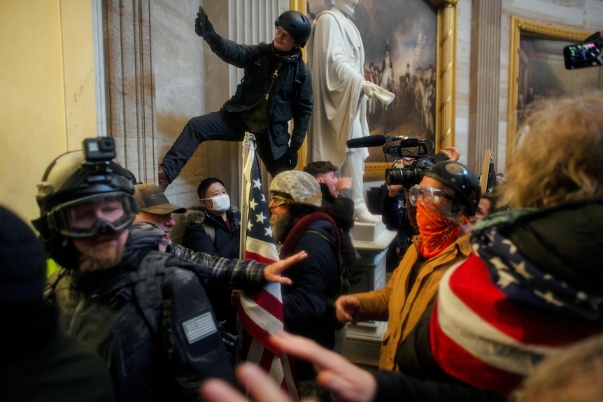 People dressed in a variety of paramilitary gear and American flags mill around in the Capitol