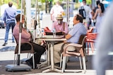 Three men, one wearing a mask, sit at an outdoor table at a Perth cafe.