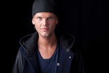 Avicci stands in front of a black background.