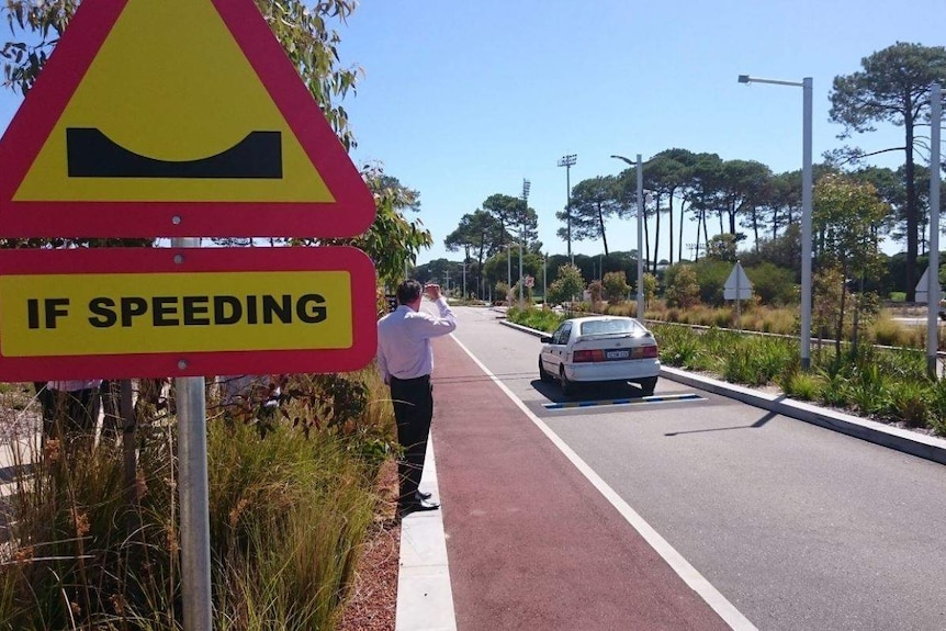 A car drives down a small road with a warning sign in the foreground.