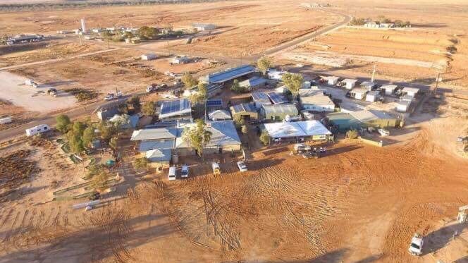 An aerial shot of a small desert town. There is red dirt surrounding all the buildings and no grass.