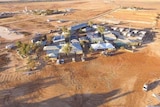 An aerial shot of a small desert town. There is red dirt surrounding all the buildings and no grass.