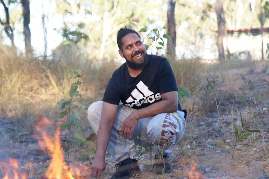 A man sits in front of a bushfire and smiles