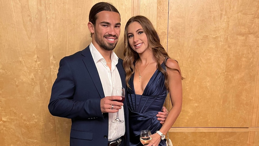 Man in dark suit smiling with wine in glass, with woman smiling in cocktail dress