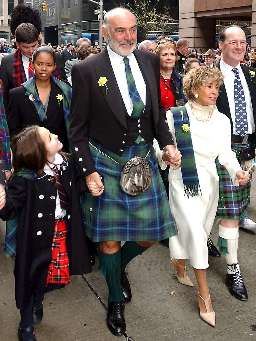 Sean Connery wearing a kilt and dress jacket walks at the front of a crowd.