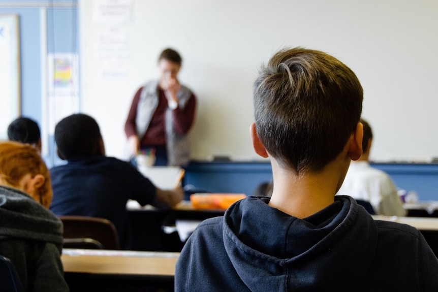 A boy faces a teacher who is standing in front of a whiteboard.