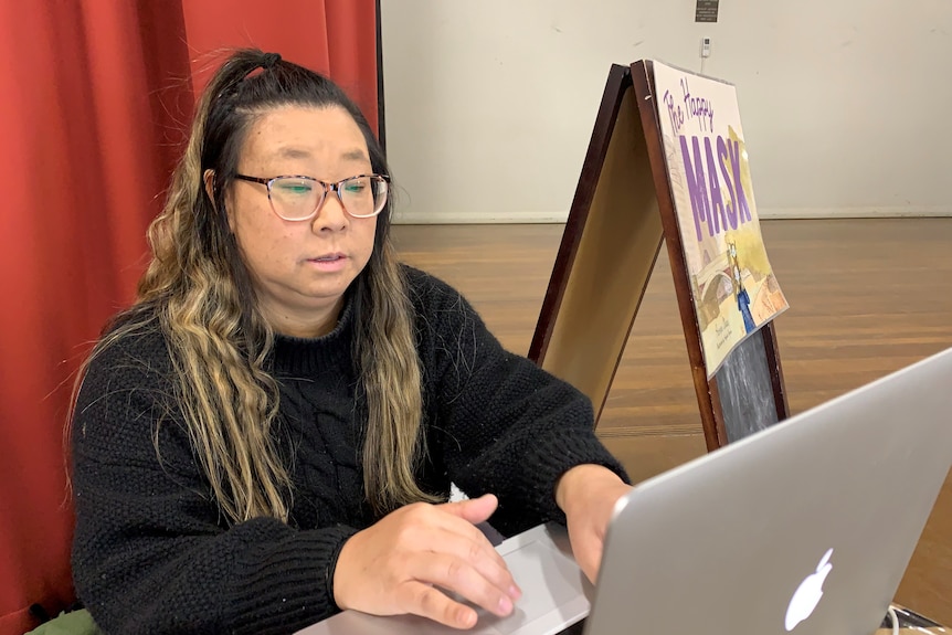 Aimee Chan sits behind a laptop on stage at Albury North Public School 