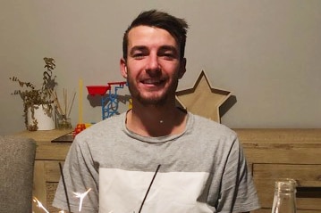 Cameron Smith smiles as he sits in front of a birthday cake.