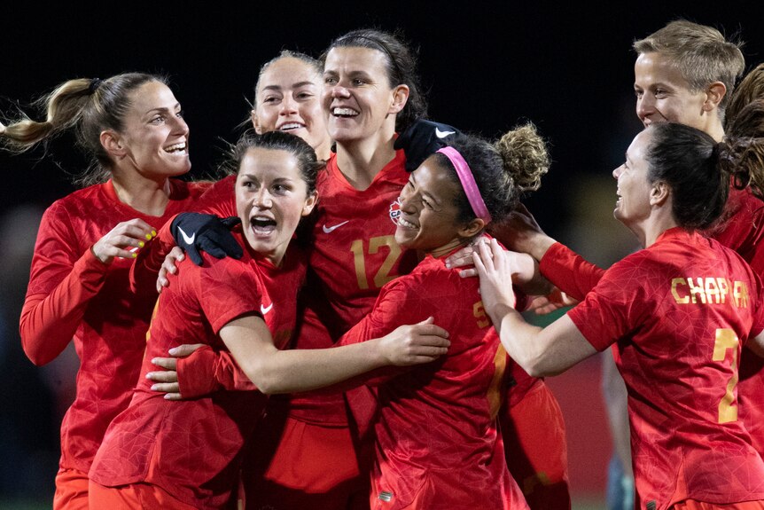 A women's soccer team wearing red celebrates after scoring a goal