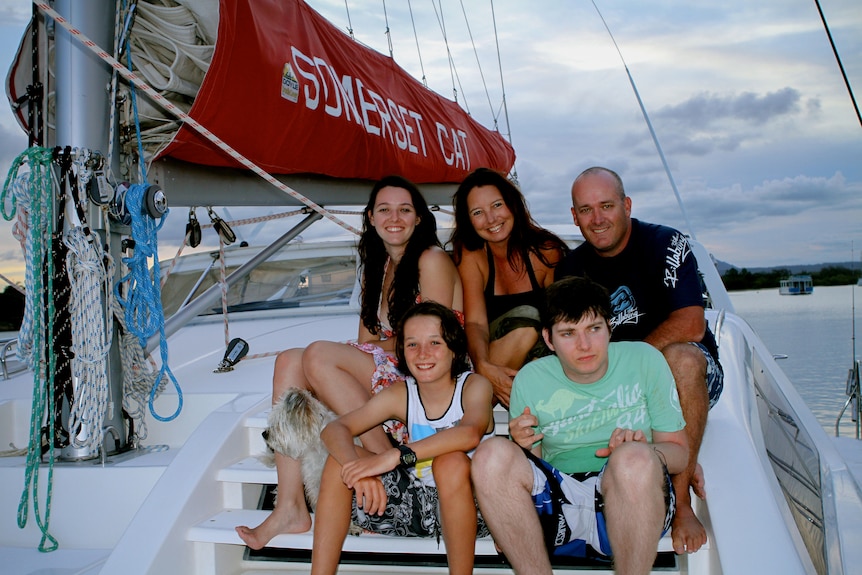 A family of five and their dog sitting together on a sailing boat.