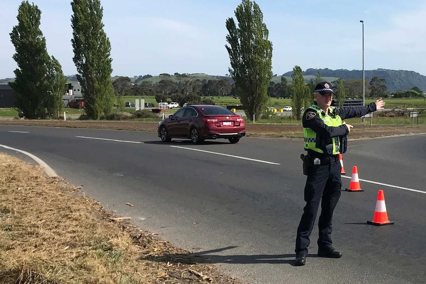 A police officer directs traffic at a roundabout in a rural area.