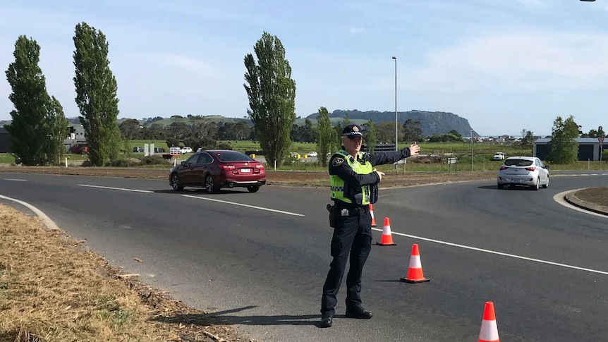 A police officer directs traffic at a roundabout in a rural area.
