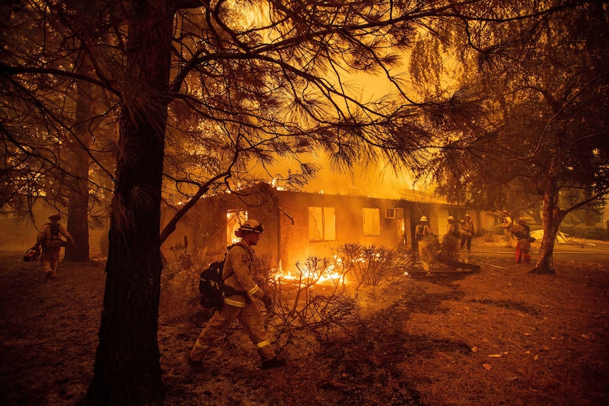 Firefighters walk through burning yard as they work to stop fire spreading through apartment complex in Paradise, California