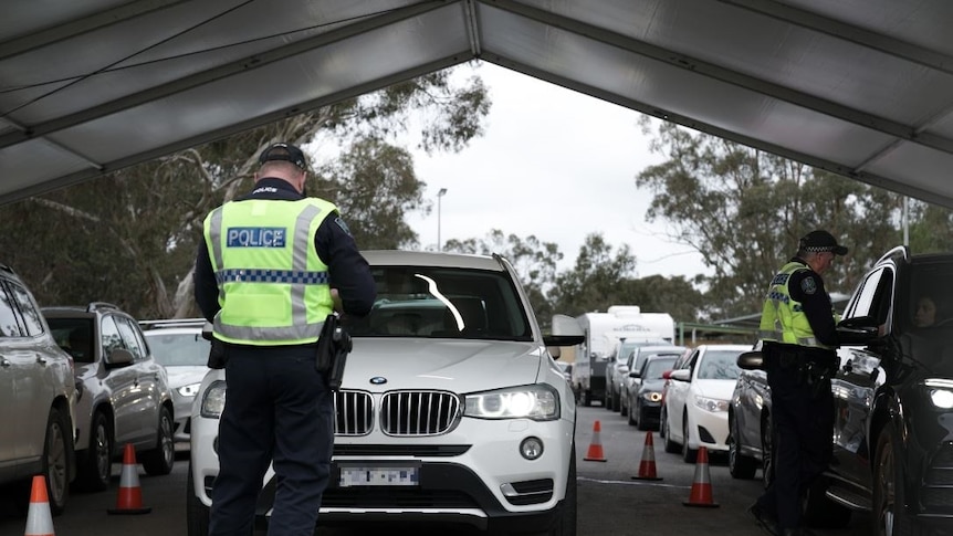 A police officer standing in front of a white four-wheel-drive with cars lined up behind it