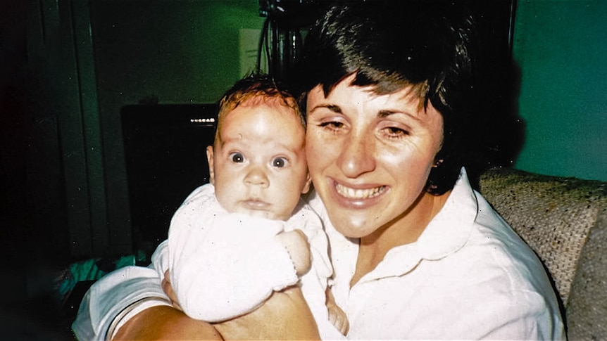 A smiling young woman holds a young, newborn baby